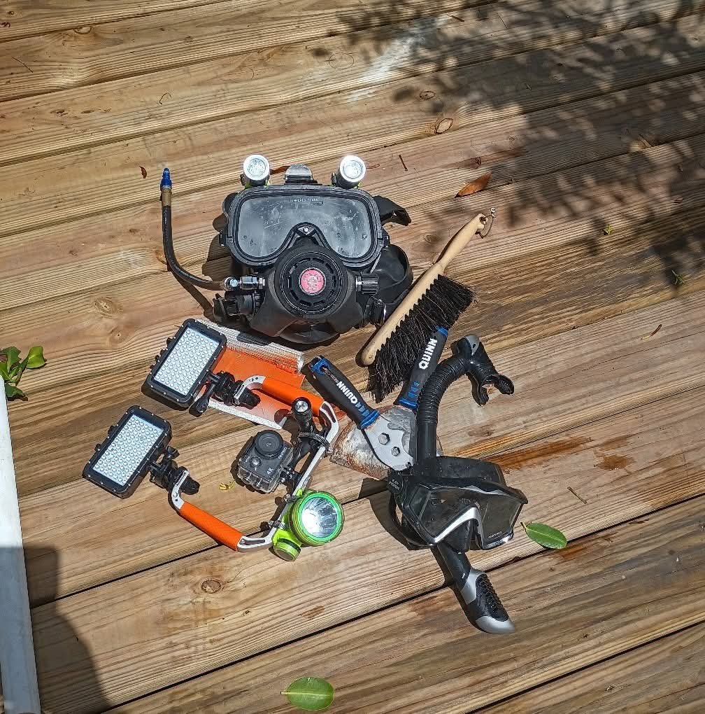 Underwater lighting, masks, camera, and cleaning tools arranged on a wooden dock